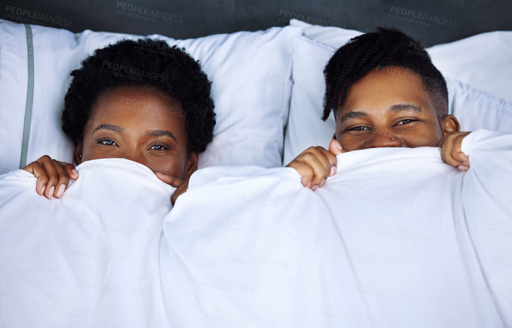 Buy stock photo Shot of a young couple hiding under the covers in bed at home