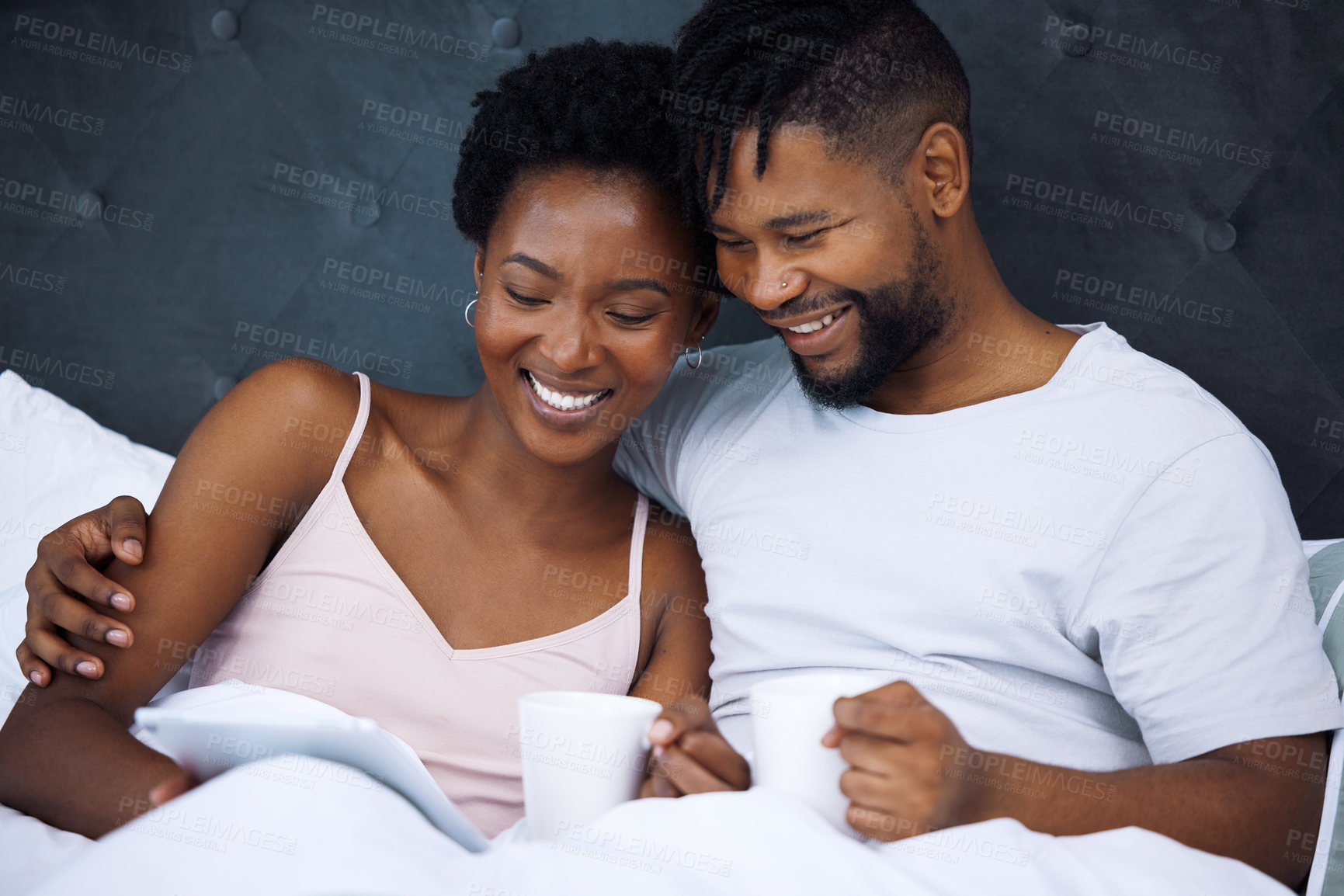 Buy stock photo Shot of a young couple using a digital tablet and having coffee in bed at home