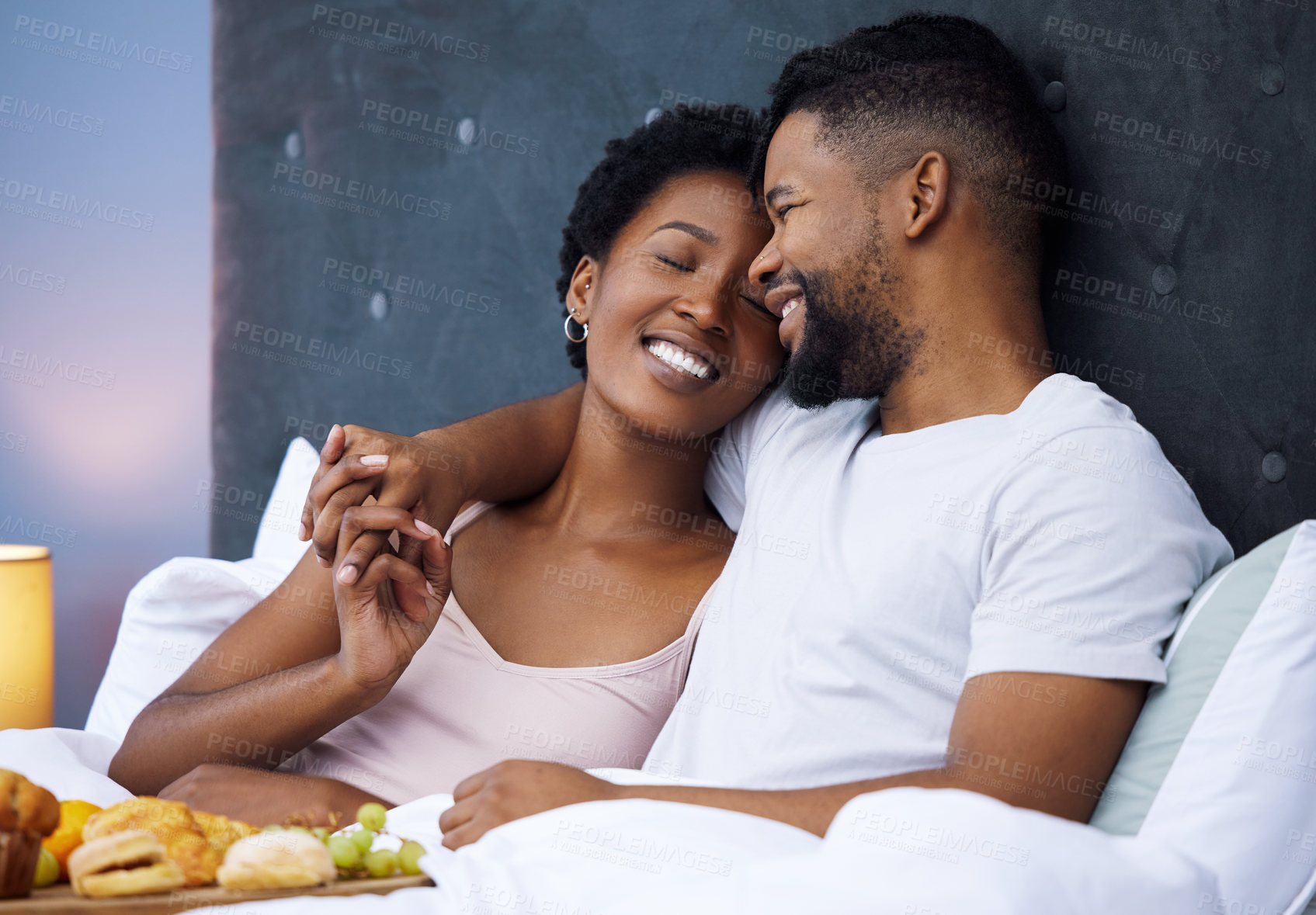 Buy stock photo Shot of a happy young couple enjoying breakfast in bed together at home