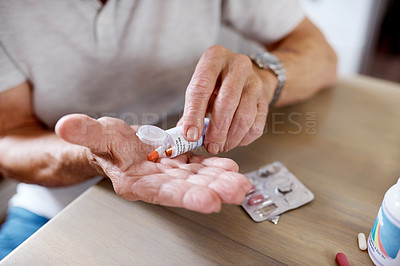 Buy stock photo Closeup shot of an unrecognizable elderly man taking medication at the kitchen table at home