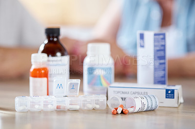 Buy stock photo Cropped shot of medication on a kitchen table with an unrecognizable couple in the background