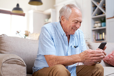 Buy stock photo Shot of an elderly man looking happy while using his smartphone at home on the sofa