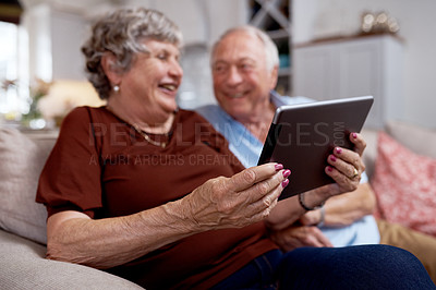 Buy stock photo Shot of an elderly couple having a laugh while using a digital tablet at home