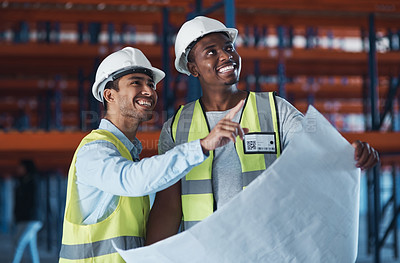 Buy stock photo Shot of two young contractors standing in the warehouse together and using a blueprint to plan