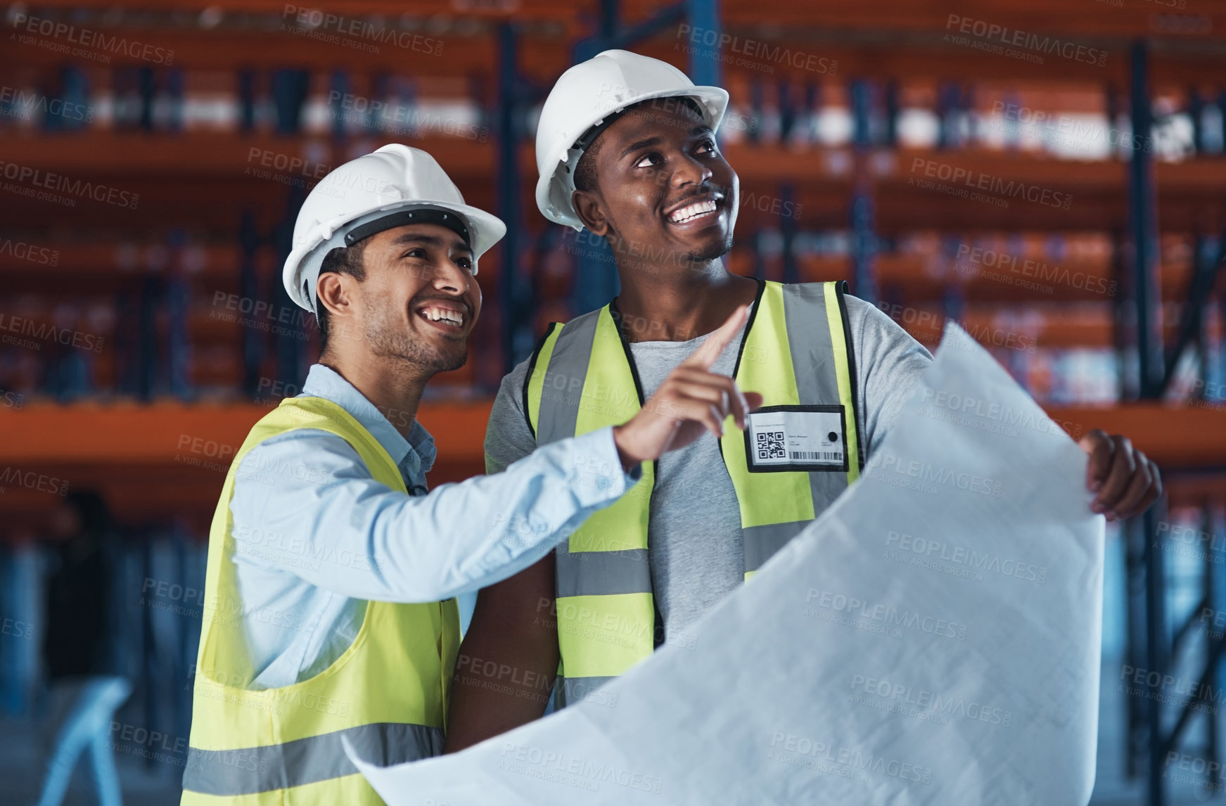 Buy stock photo Shot of two young contractors standing in the warehouse together and using a blueprint to plan