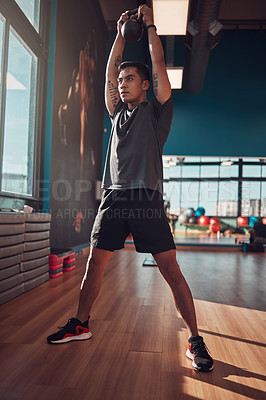 Buy stock photo Shot of a young man working out using a kettlebell in the gym