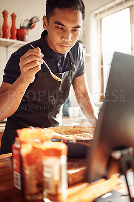 Buy stock photo Shot of a young man using a laptop while preparing a meal at home