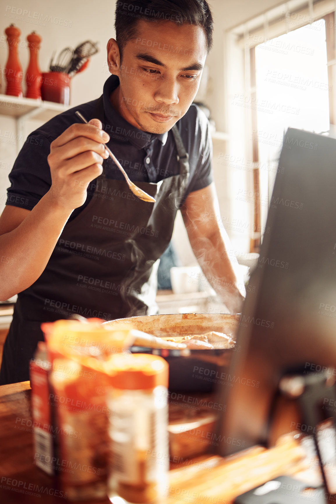 Buy stock photo Shot of a young man using a laptop while preparing a meal at home