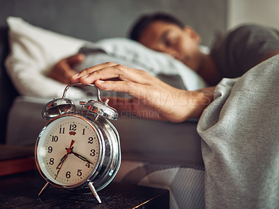 Buy stock photo Shot of a young man reaching for his alarm clock after waking up in bed at home