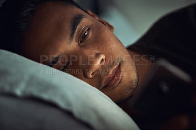 Buy stock photo Shot of a young man lying in bed and using a smartphone at home