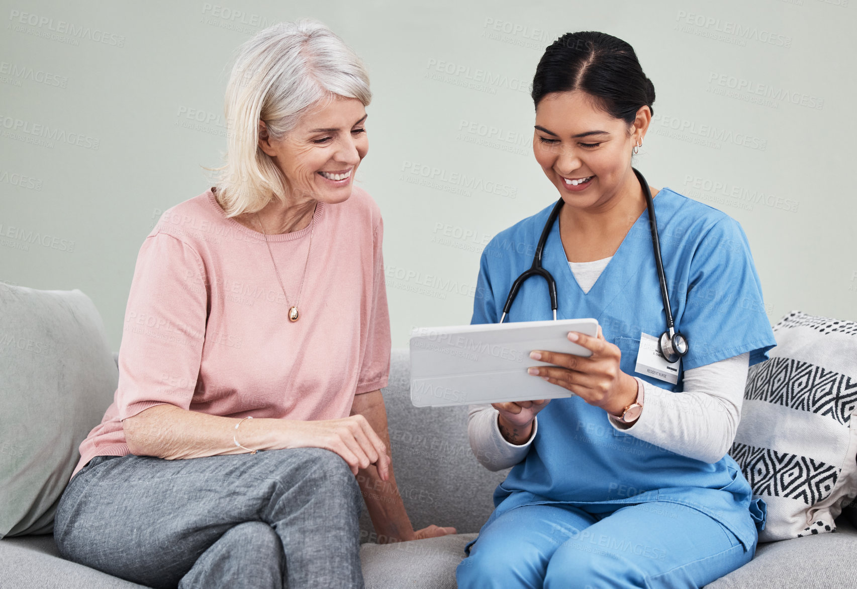 Buy stock photo Shot of a female nurse using a digital tablet while sitting with her patient