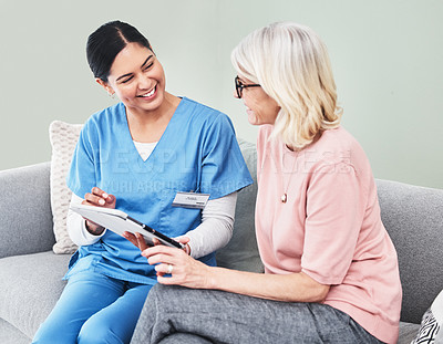 Buy stock photo Shot of a female nurse using a digital tablet while sitting with her patient
