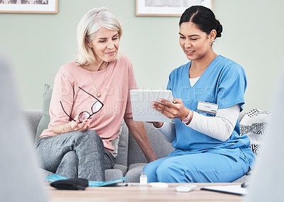 Buy stock photo Shot of a female nurse using a digital tablet while sitting with her patient