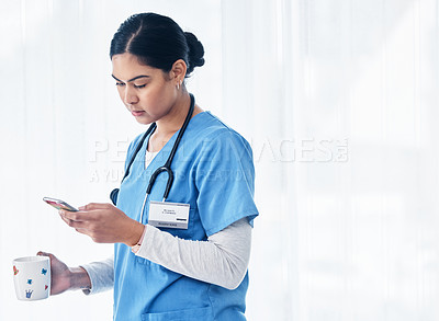 Buy stock photo Shot of a female nurse holding a cup of coffee while using her cellphone