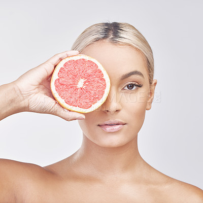 Buy stock photo Studio shot of a beautiful young woman holding a grapefruit in front of her eye against a grey background