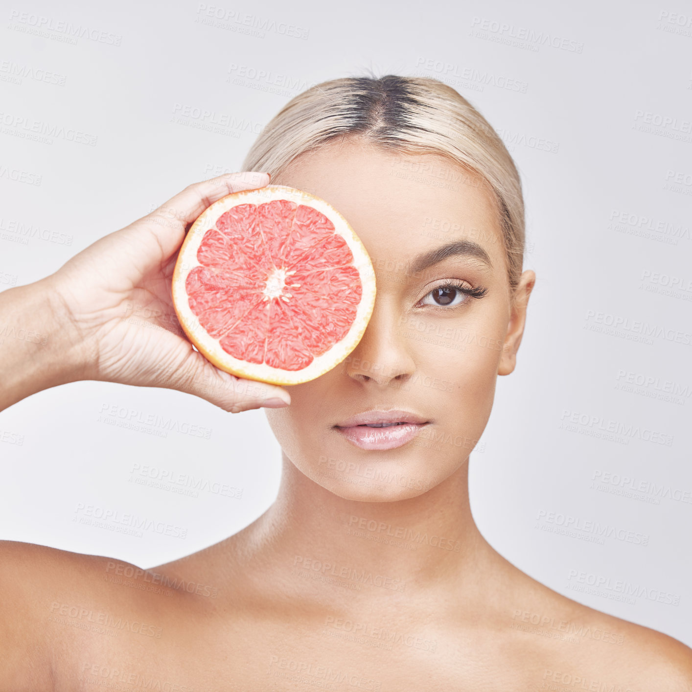 Buy stock photo Studio shot of a beautiful young woman holding a grapefruit in front of her eye against a grey background