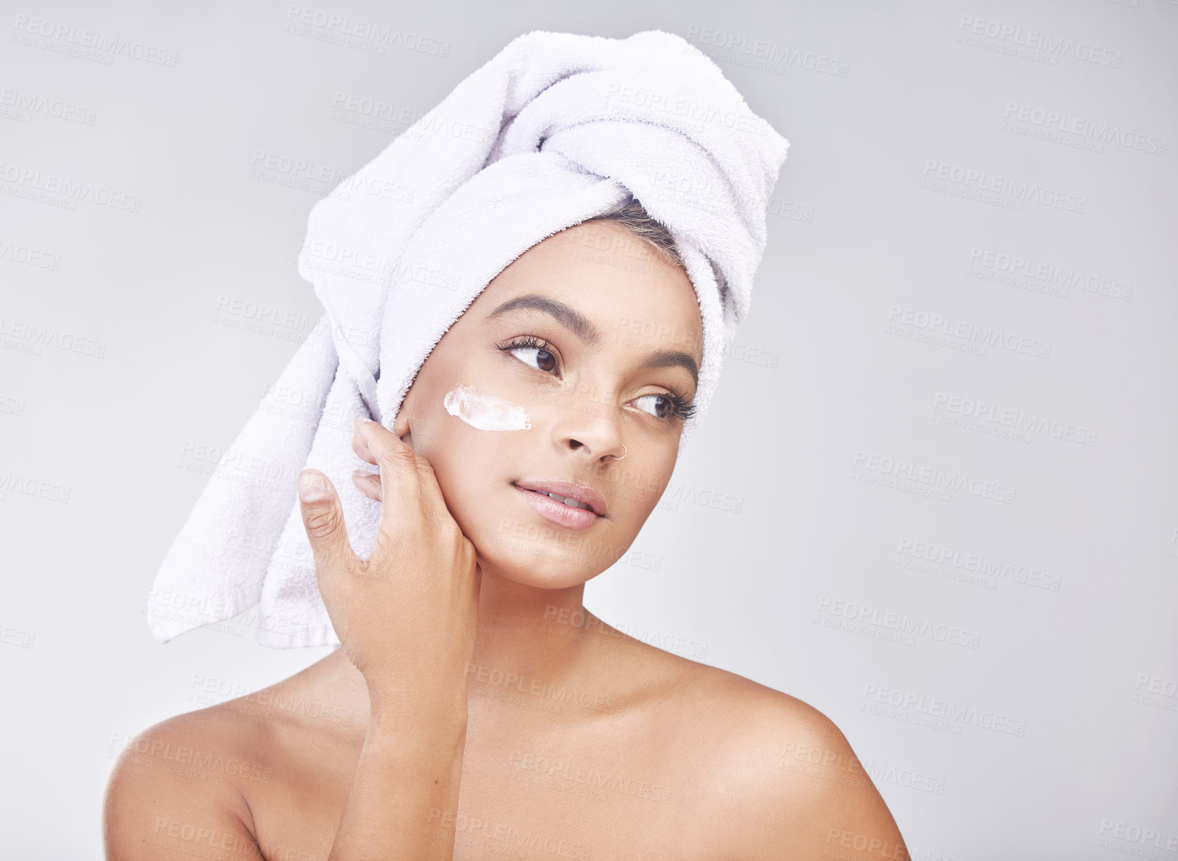 Buy stock photo Studio shot of a beautiful young woman applying moisturiser against a grey background