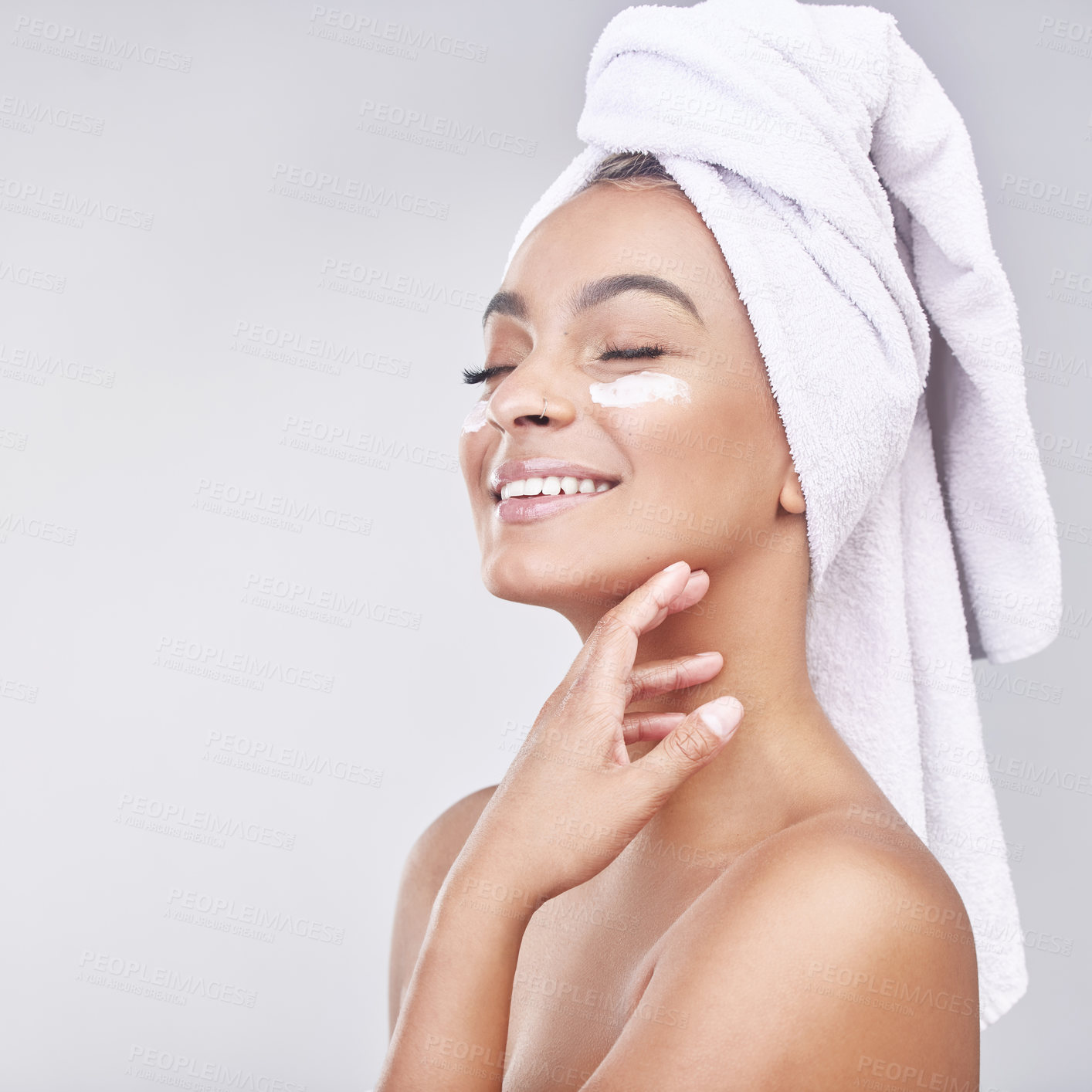 Buy stock photo Studio shot of a beautiful young woman applying moisturiser against a grey background