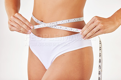 Buy stock photo Shot of a model measuring herself using tape measure against a studio background
