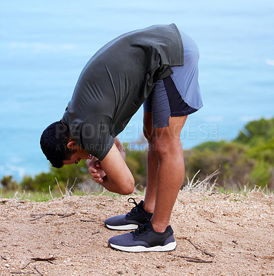 Buy stock photo Shot of a sporty young man bending down in a stretch while exercising outdoors