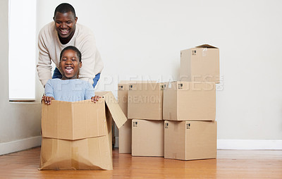 Buy stock photo Shot of a happy young father bonding with his daughter and pushing her in a box in their new home