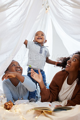 Buy stock photo Shot of an attractive young woman lying down with her children at home under a sheet fort