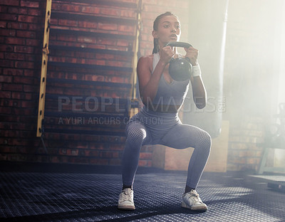 Buy stock photo Shot of a sporty young woman doing kettlebell squats in a gym