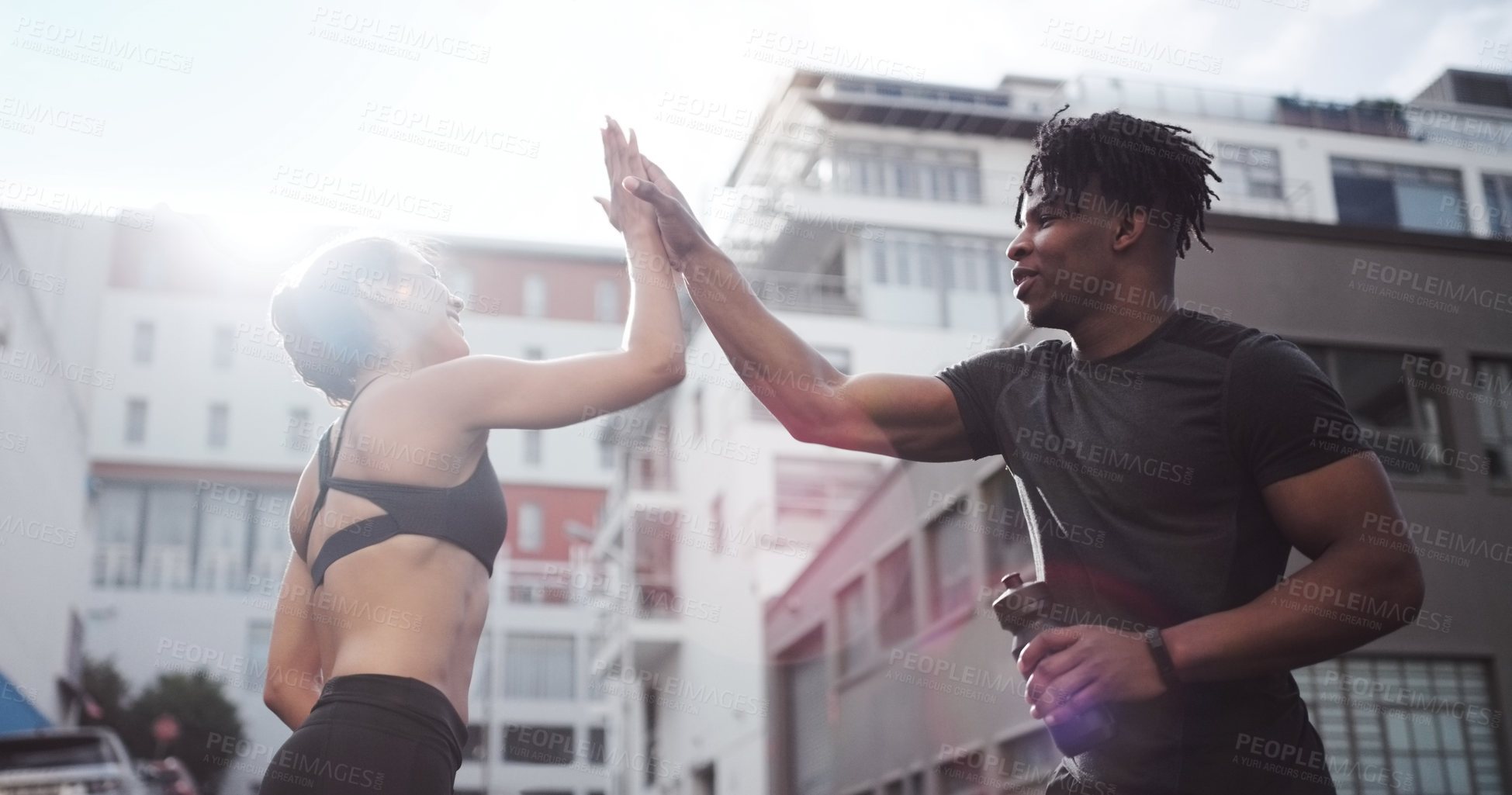 Buy stock photo Shot of a young couple giving each other a high-five while standing outside in sportswear