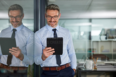 Buy stock photo Shot of a mature man using his digital tablet while leaning against n office window at work