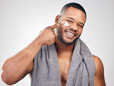 Buy stock photo Studio portrait of a handsome young man applying moisturiser to his face against a white background