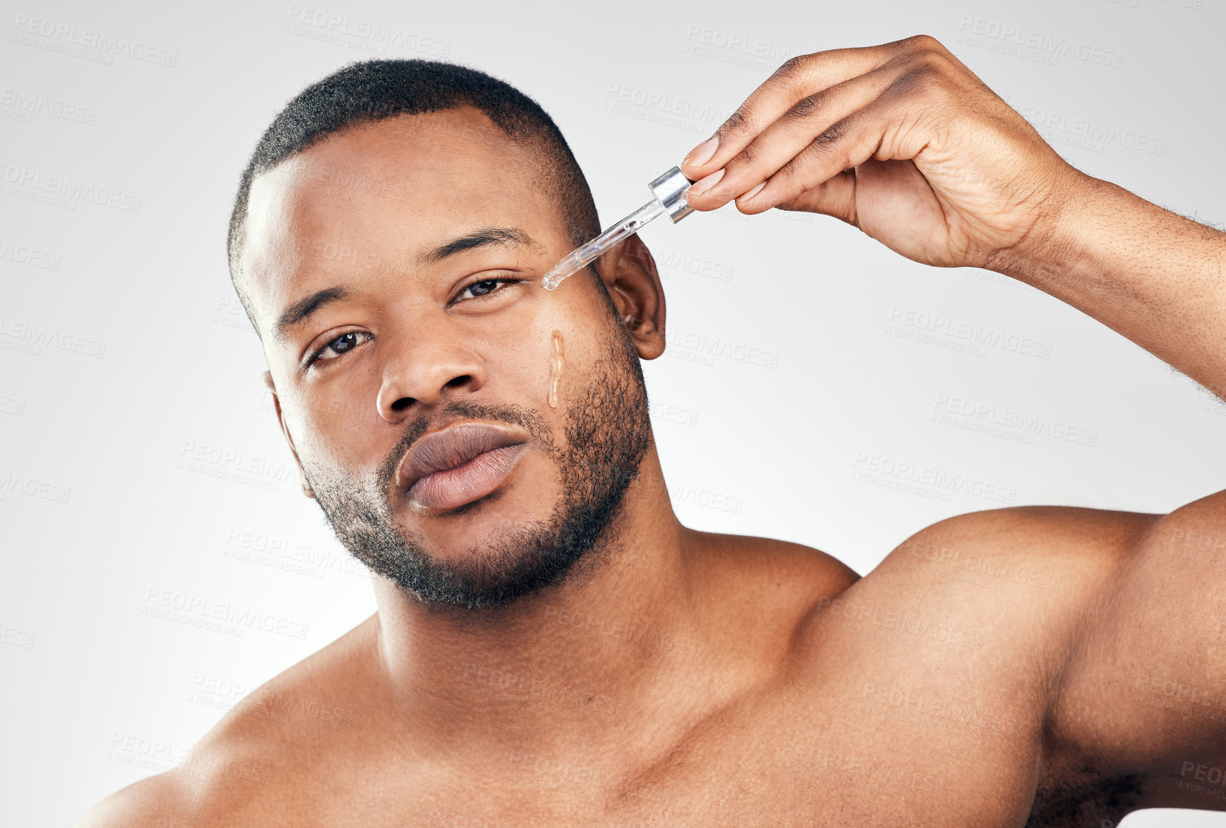 Buy stock photo Studio portrait of a handsome young man applying serum to his face with a dropper against a white background