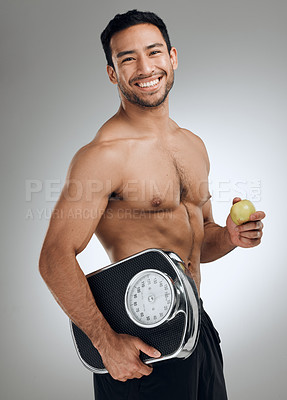 Buy stock photo Shot of an athletic young man holding an apple and a weighing scale