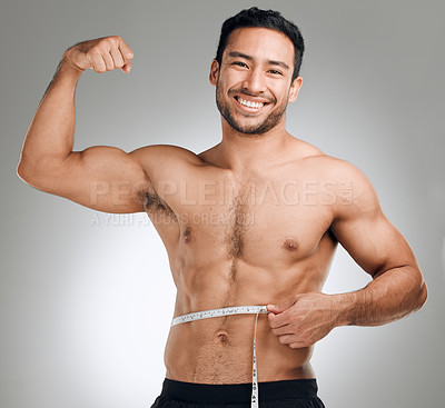Buy stock photo Studio shot of a man flexing his muscles while measuring his waist