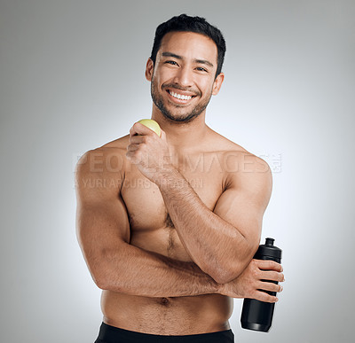 Buy stock photo Shot of a man standing against a grey background while holding a bottle of water and an apple