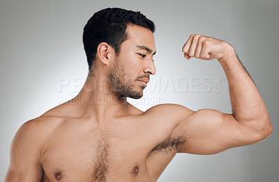 Buy stock photo Shot of a young man flexing his muscles while standing against a grey background