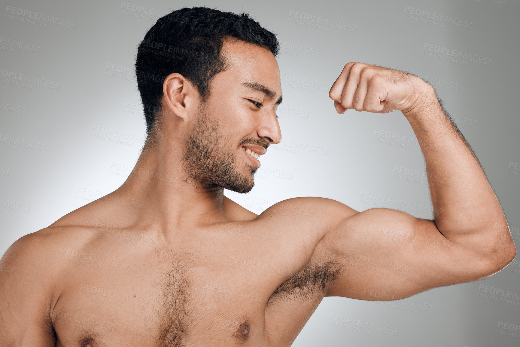 Buy stock photo Shot of a young man flexing his muscles while standing against a grey background