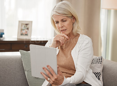 Buy stock photo Shot of a mature woman using a digital tablet and looking concerned at home