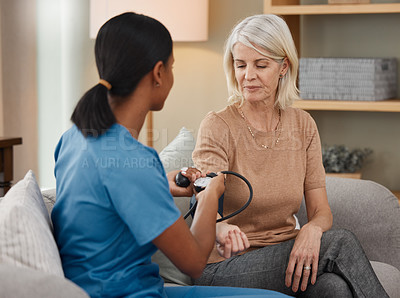 Buy stock photo Shot of a doctor examining a senior woman with a blood pressure gauge at home