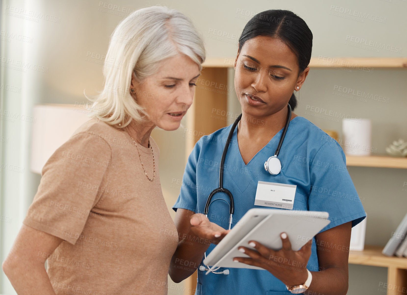 Buy stock photo Shot of a doctor using a digital tablet during a consultation with a senior woman at home