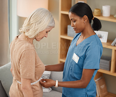 Buy stock photo Shot of a doctor using a measuring tape on a senior woman’s stomach during a consultation at home