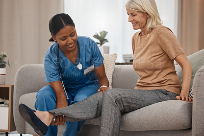 Buy stock photo Shot of a doctor examining a senior woman’s ankle on the sofa at home