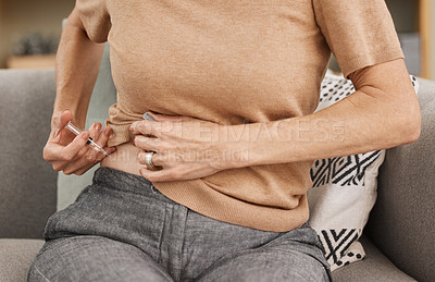 Buy stock photo Shot of a mature woman injecting herself with insulin on the sofa at home