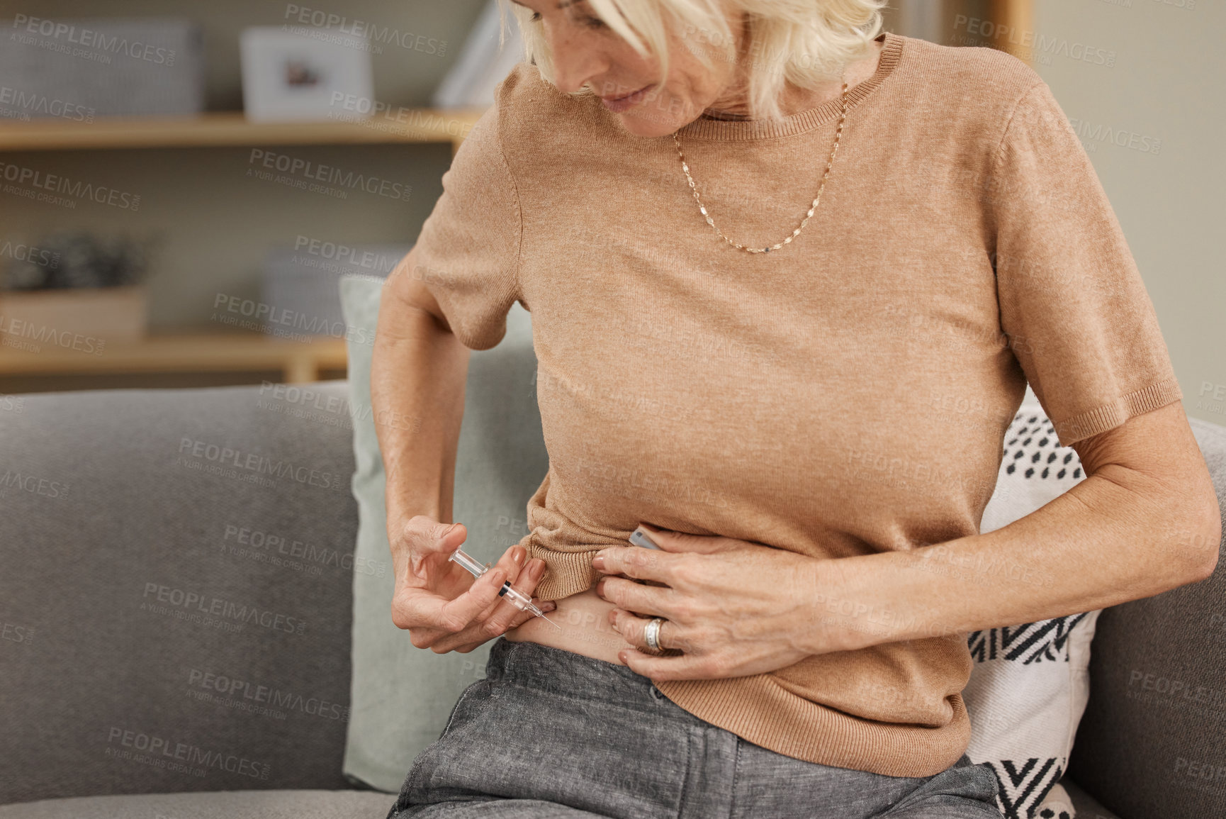 Buy stock photo Shot of a mature woman injecting herself with insulin on the sofa at home