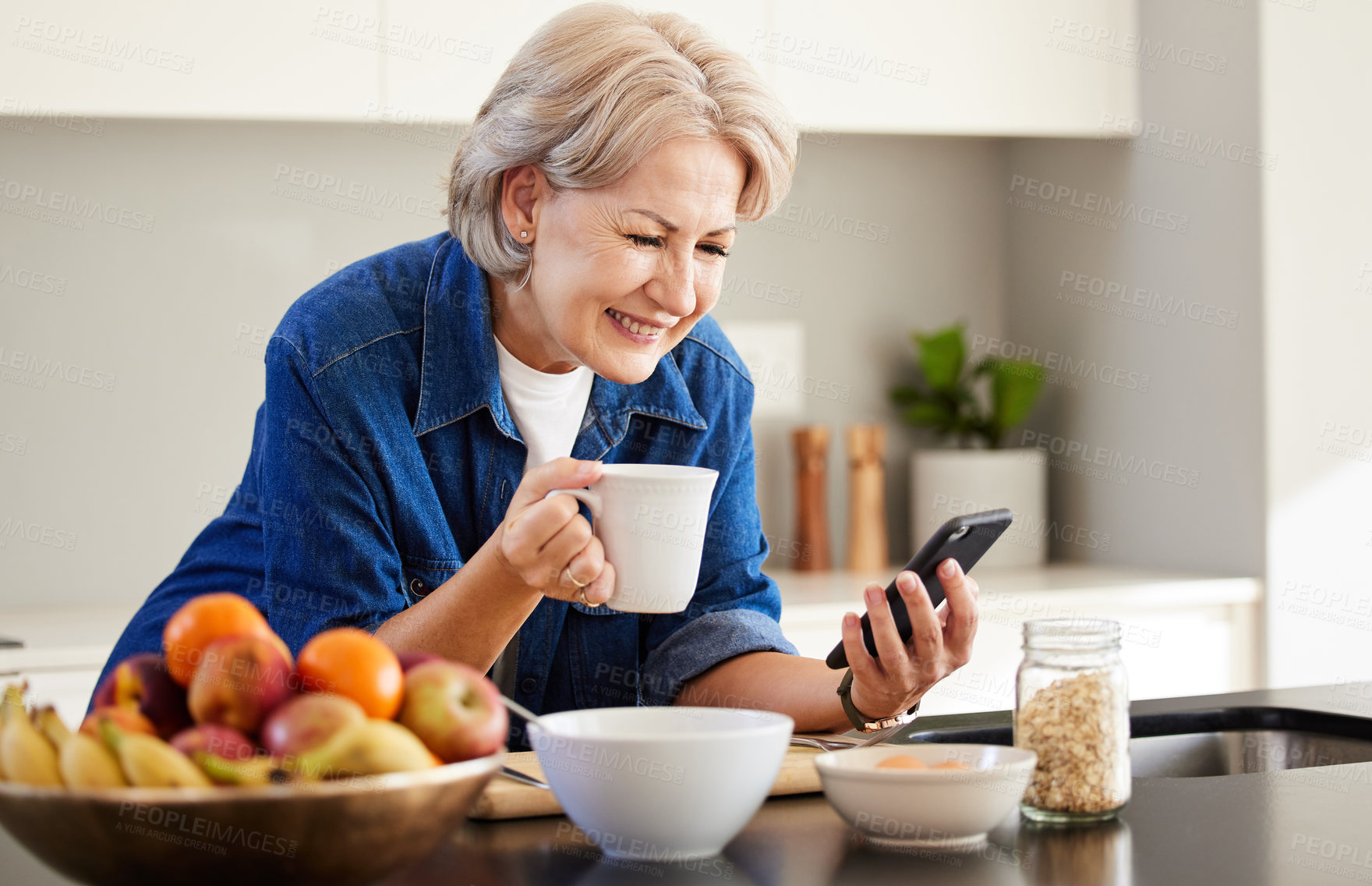 Buy stock photo Shot of a senior woman using her cellphone and drinking coffee at home