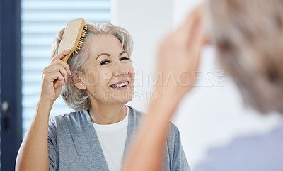 Buy stock photo Shot of a senior woman brushing her hair while looking in her bathroom mirror