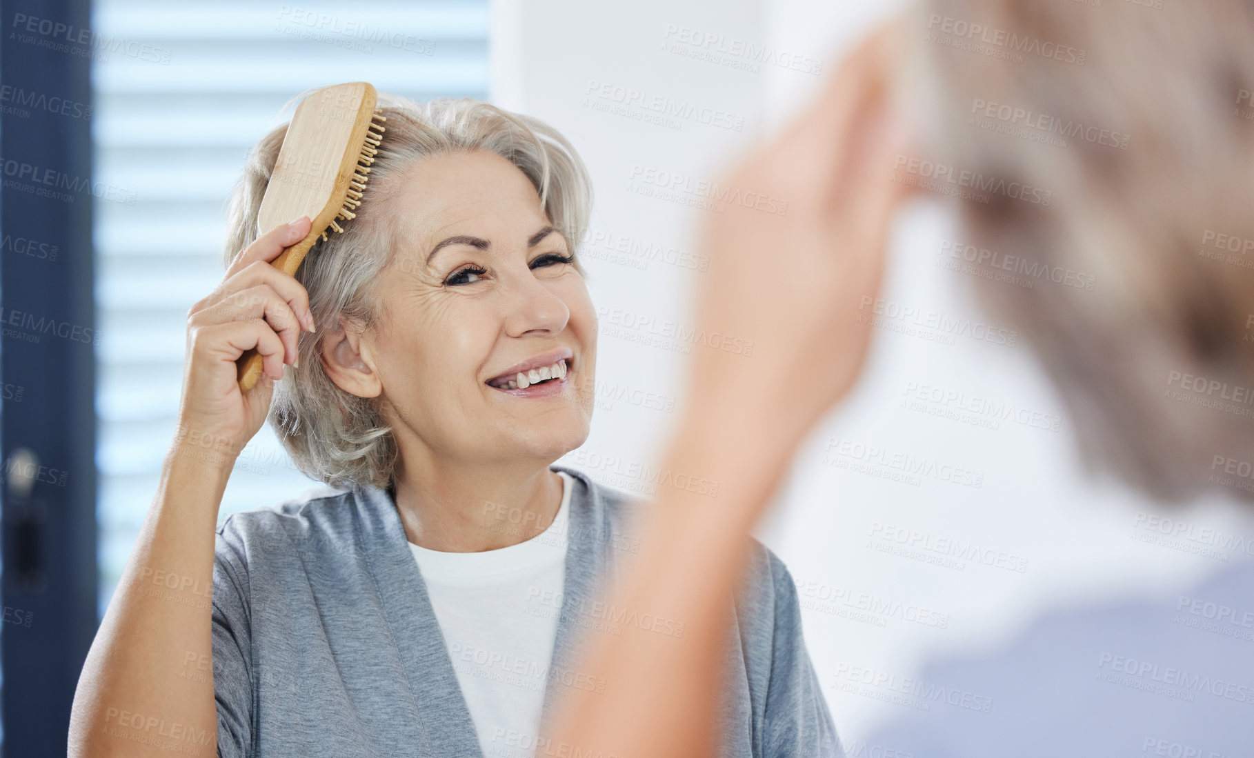 Buy stock photo Shot of a senior woman brushing her hair while looking in her bathroom mirror