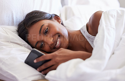 Buy stock photo Shot of a young woman using her cellphone while lying in her bed