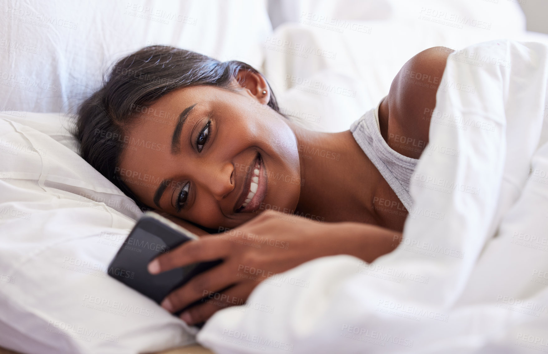 Buy stock photo Shot of a young woman using her cellphone while lying in her bed