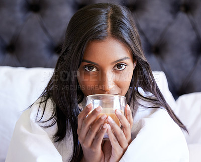 Buy stock photo Shot of a young woman drinking a hot beverage while sitting on her bed