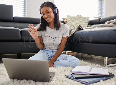 Buy stock photo Shot of a young woman sitting in her living room and wearing headphones while using her laptop for a video call